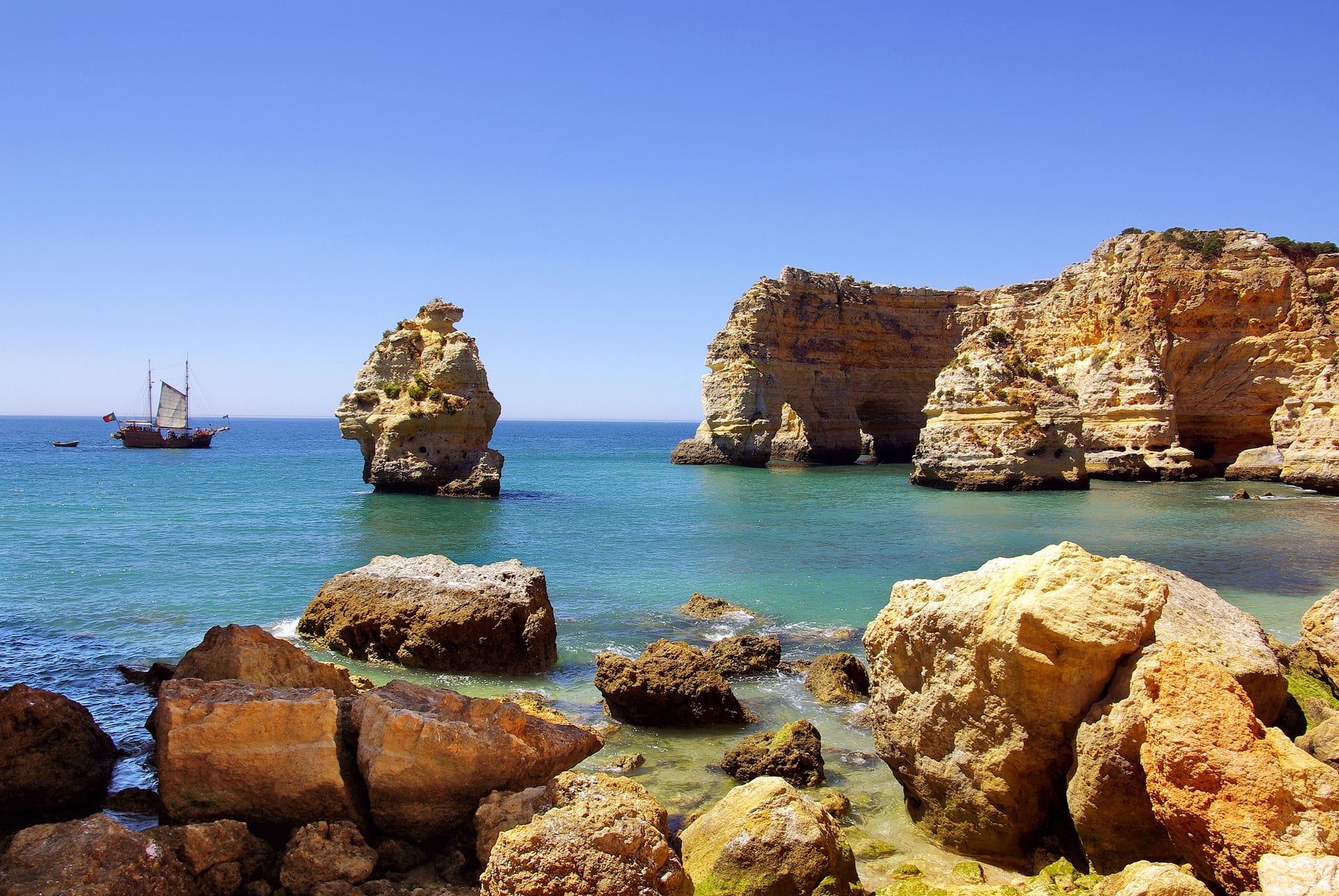 Goldene Felsformationen der Algarve-Küste in Portugal mit türkisblauem Atlantik und Segelboot.