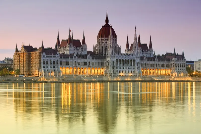 Das beleuchtete ungarische Parlamentsgebäude spiegelt sich in der Donau bei Sonnenuntergang in Budapest.