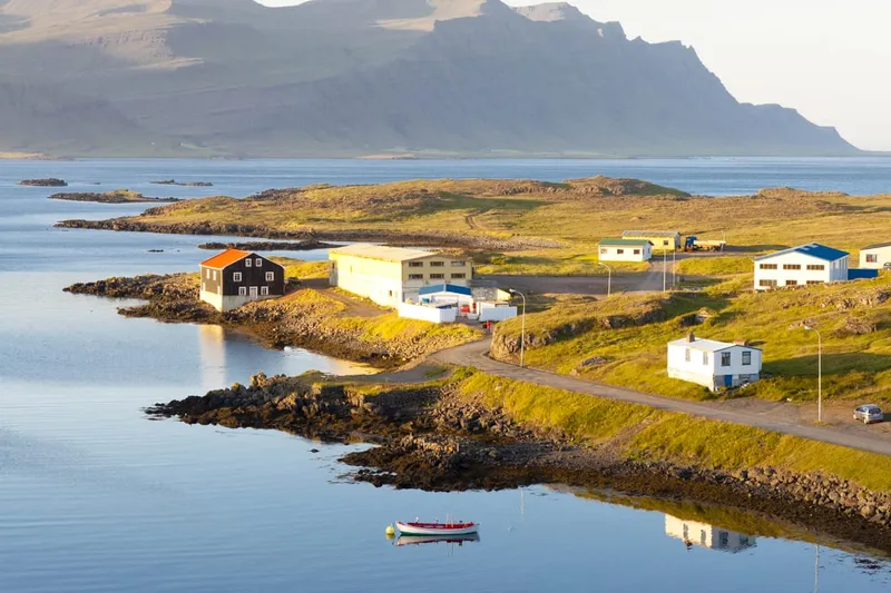 Kleines Fischerdorf Djupivogur auf Island mit ruhigem Fjordwasser, einem kleinen Boot im Vordergrund und Basaltbergen im Hintergrund