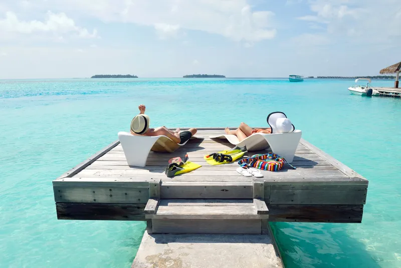 Paar entspannt auf einem Holzsteg über türkisblauem Meer auf den Malediven mit Schnorchelausrüstung.