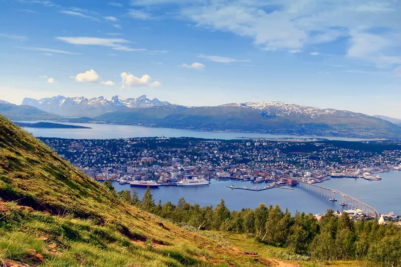 Panoramablick auf Tromsø in Norwegen mit Hafen, Kreuzfahrtschiff und schneebedeckten Bergen im Hintergrund.